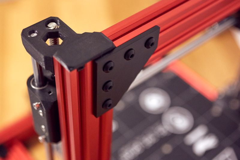A detailed view of the top of the Prusa Bear Upgrade 2.1 3D printer, showing the red aluminium extrusions and black printed parts. The top of the Z-axis and the end of the X-axis are visible